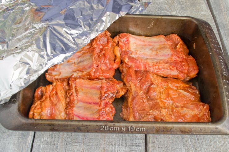 Baking Pork Ribs in a Dish Covered with Foil Marinated pork ribs arranged in a baking dish and covered with a sheet of aluminum foil.