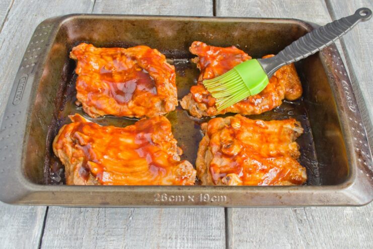 Applying the Honey Glaze to the Ribs Before Final Roasting A kitchen brush glazing partially cooked pork ribs with a thick, dark honey sauce.