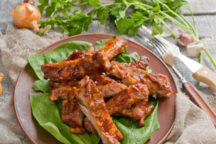 Serving Suggestion: Cutting Cooked Ribs into Individual Portions Cooked, glazed pork ribs on a cutting board being sliced into individual portions for serving.