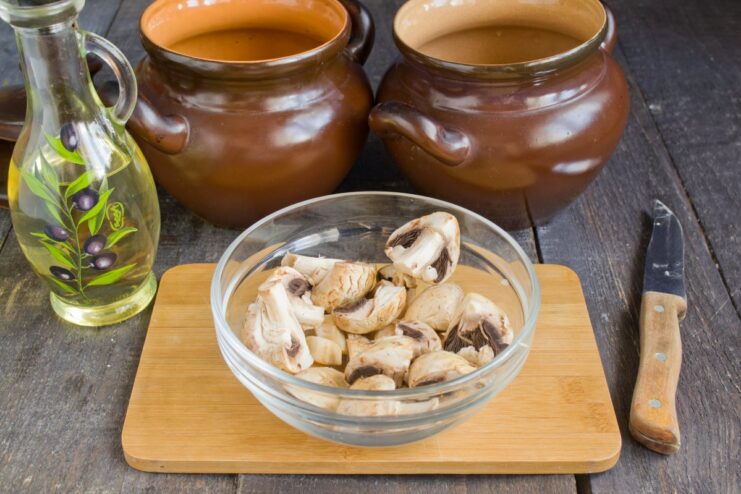 Adding Earthy Flavors: Layering Mushrooms Over the Pork Ribs Marinated pork ribs in clay pots topped with a layer of whole and sliced champignon mushrooms.