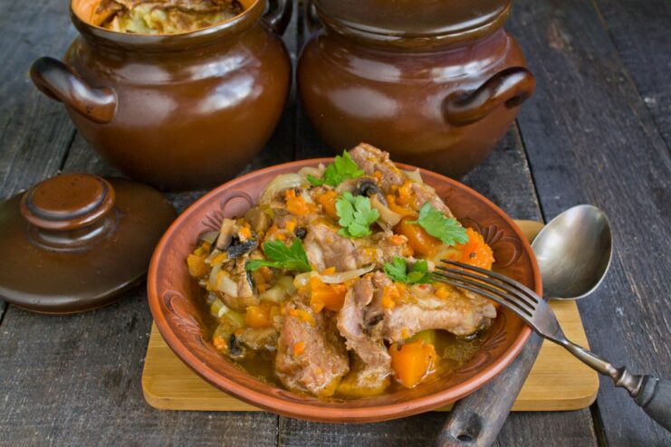 Ready to Serve: Hot and Aromatic Pork Ribs Straight from the Oven A finished dish of pork ribs with pumpkin and mushrooms served in a clay pot, garnished with parsley.