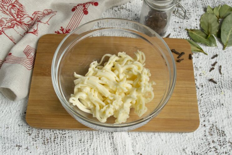 Grating Butter and Processed Cheese for the Appetizer Base A hand grating a block of processed cheese and cold butter into a glass bowl.