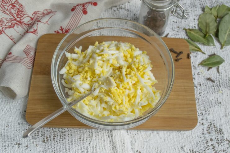 Adding Grated Eggs to the Cheese Mixture Grated hard-boiled eggs being added to the bowl with grated cheese and butter.