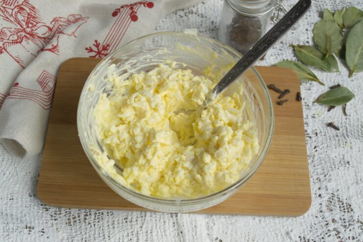 Mixing the Cheese Salad Until Well Combined A spoon mixing the cheese, egg, and mayonnaise salad in a glass bowl.