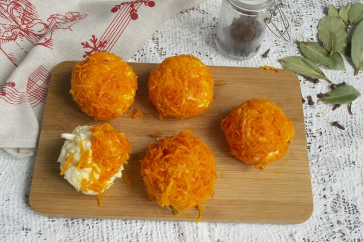 Coating the Cheese Balls in the Carrot Mixture A cheese ball being carefully rolled in the cooked carrot mixture to create a 'tangerine'.