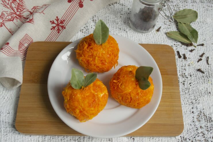 Garnishing with Bay Leaves to Resemble Tangerine Stems A hand inserting a small bay leaf into the top of a carrot-coated cheese ball.