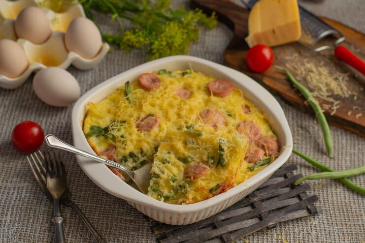 A slice of hearty vermicelli casserole with sausages and green beans on a plate, ready to eat.