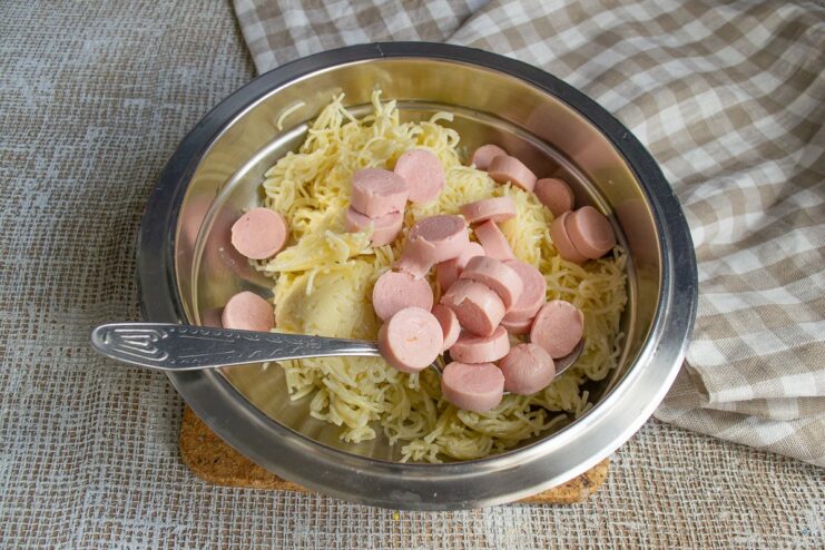 Combining pasta and sausages for the casserole filling. A bowl with cooked vermicelli and sliced sausages being mixed together.
