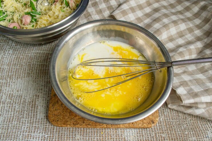 Making the egg and milk custard for the casserole. Pouring milk into a bowl of whisked eggs.