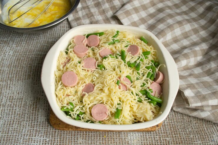 Assembling the vermicelli casserole in a baking dish. A baking dish being filled with the vermicelli, sausage, and green bean mixture.