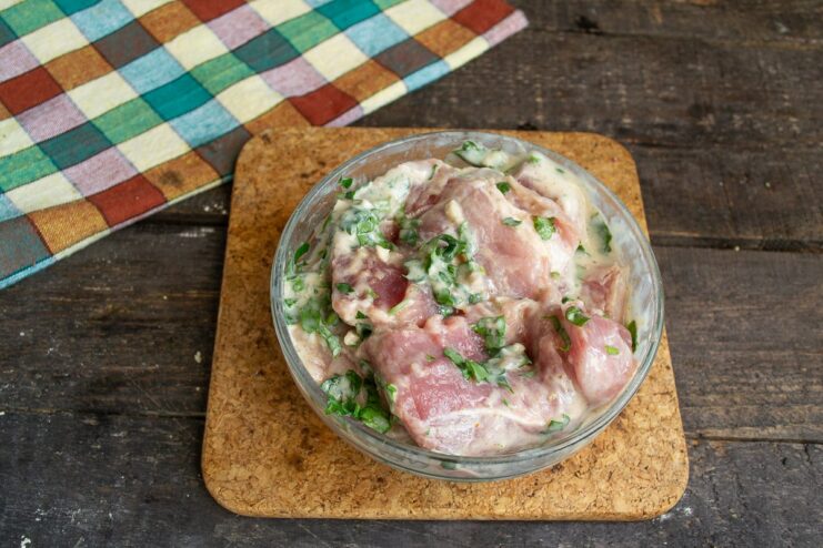 Marinating the meat in yogurt and spices makes it incredibly tender and flavorful. Raw meat in a bowl being mixed with a yogurt-based marinade, parsley, and garlic.