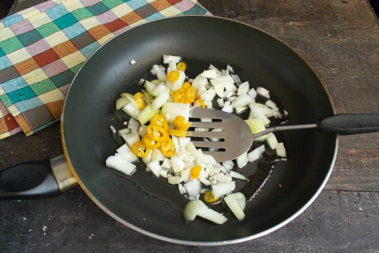Sautéing aromatics like onion, garlic, ginger, and chili builds the flavor base for the curry. Chopped onion, garlic, ginger, and chili being sautéed in a pan with melted ghee.