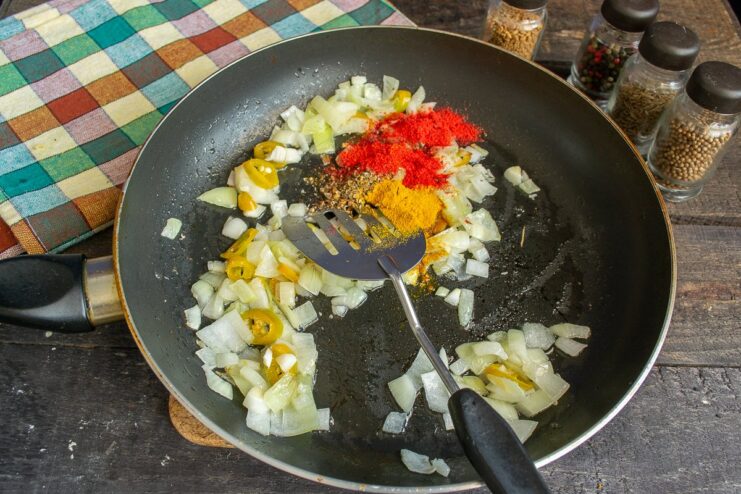 Toasting the spices with the vegetables awakens their essential oils and deepens the flavor. Sautéed vegetables in a pan with ground spices being stirred.