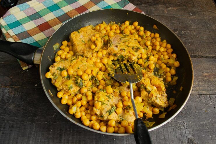 Fresh cilantro adds a burst of freshness that cuts through the richness of the curry. Finished chickpea curry in a pan being garnished with a generous amount of fresh chopped cilantro.