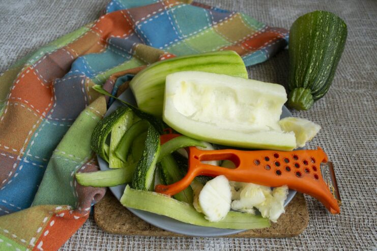 Step 1: Preparing the zucchini by peeling the outer skin. A person peeling a large green zucchini with a vegetable peeler.