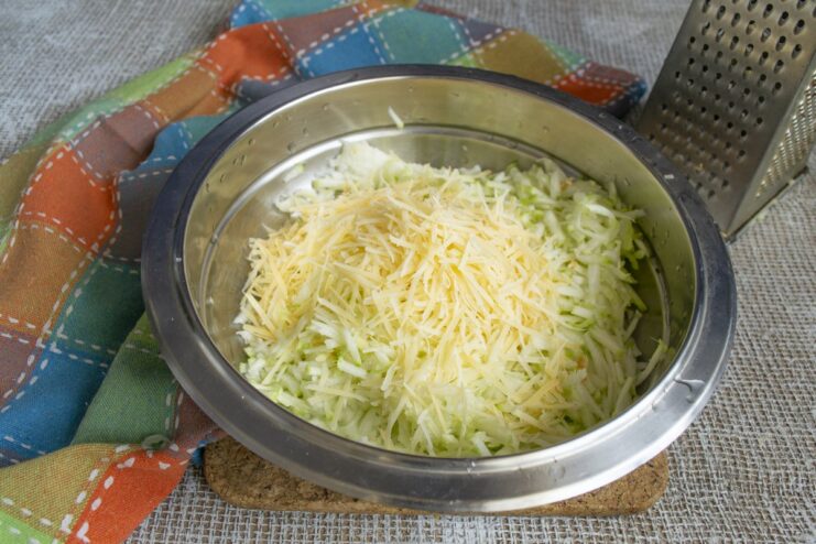 Adding savory grated Parmesan cheese to the shredded zucchini. Grated Parmesan cheese being added to a bowl of shredded zucchini.