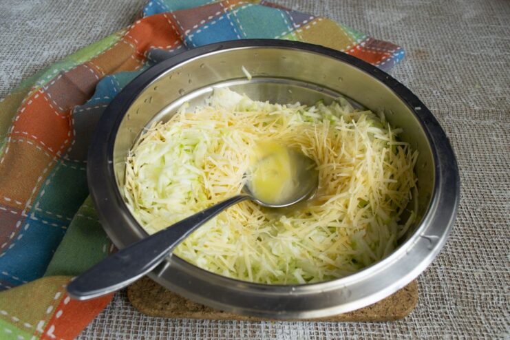 Binding the fritter batter by adding two fresh eggs to the zucchini and Parmesan mixture. Two eggs cracked into a bowl with shredded zucchini and Parmesan cheese.