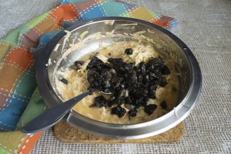 Incorporating the cooked mushrooms and onions into the zucchini batter. Cooked mushrooms and onions being mixed into the zucchini fritter batter in a bowl.