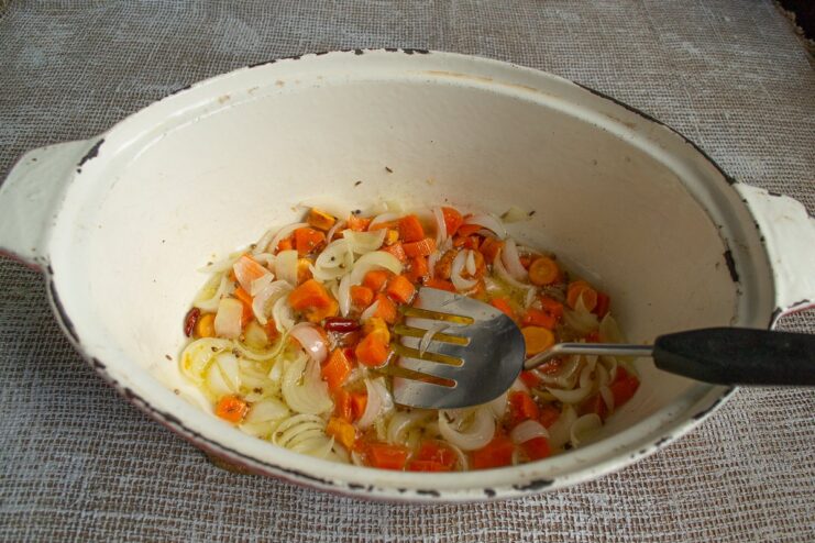 Simmering Vegetables Until Soft and Fragrant Onions and carrots simmering in oil and spices in a cast-iron pan.