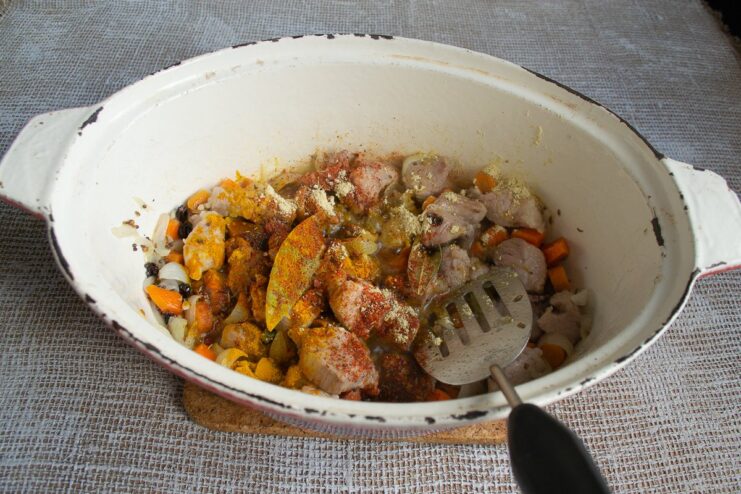 Adding the Final Layer of Spices for a Rich Plov A variety of ground spices and barberries being added to the meat and vegetables in the pan.