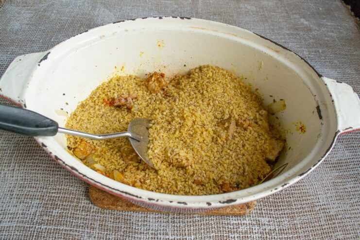 Layering Bulgur Over the Meat and Vegetables Dry bulgur being spread evenly over the seared pork and vegetables in a pan.