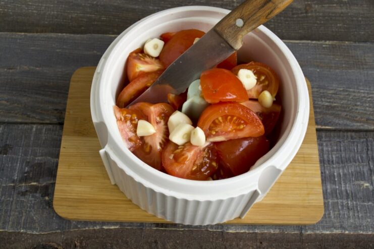 Adding fresh tomatoes and garlic to the blender for a flavorful sauce base. Chopped tomatoes and garlic cloves added to the bell peppers in the blender bowl.