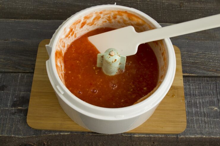Blending the vegetables into a smooth puree and simmering it to thicken the sauce. Smooth red vegetable puree being poured from a blender into a saucepan on the stove.