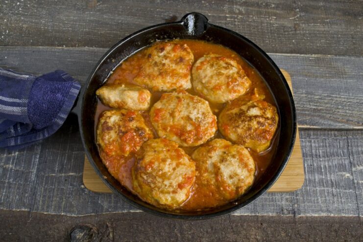 Simmering the golden-brown meatballs in the rich tomato sauce to cook them through. Hot tomato and pepper sauce being poured over fried meatballs in a pan for simmering.