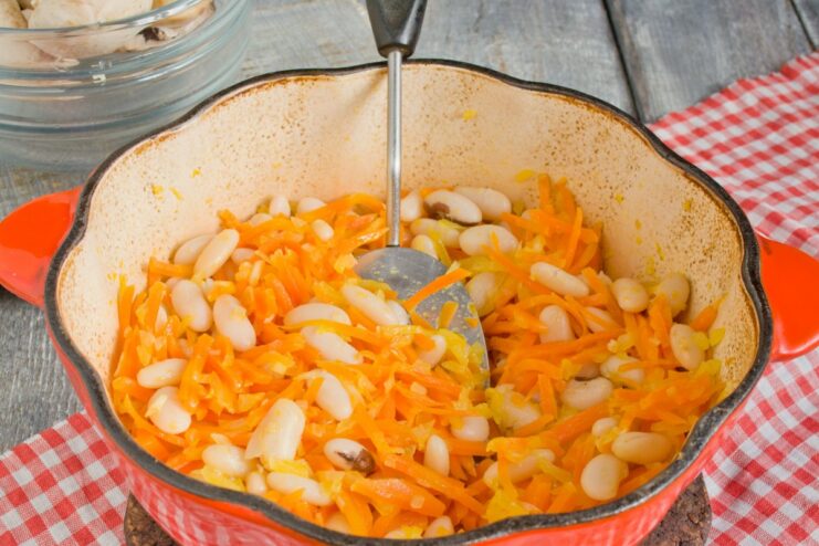 Combining Sautéed Vegetables with Cooked Beans Cooked beans being added to a pot with sautéed onions and carrots.