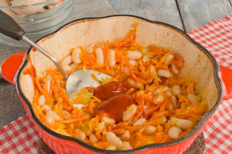 Adding Ketchup for a Rich Tomato Flavor Ketchup being added from a spoon into the pot with beans and vegetables.