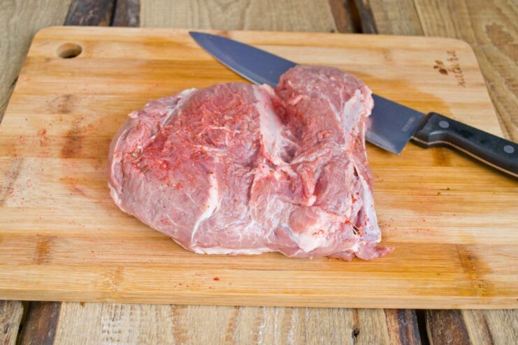 Seasoning the Pork with Ground Red Pepper Before Cooking A raw piece of pork on a cutting board being seasoned with ground red pepper.