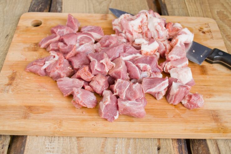 Cutting Pork into Cubes for Braising Close-up of pork being cut into evenly sized cubes on a cutting board.