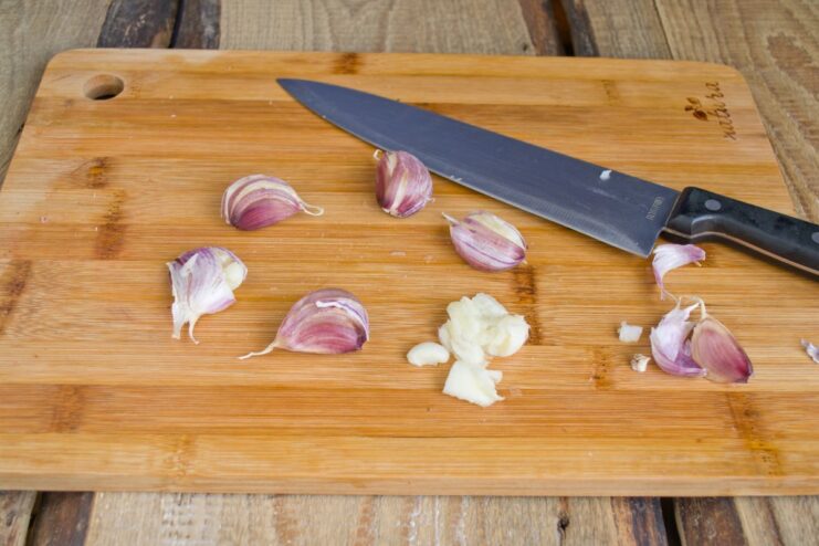 How to Easily Peel and Mince Garlic for Maximum Flavor Garlic cloves being crushed with the flat side of a knife before mincing.