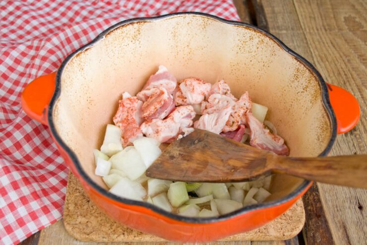 Layering Onions, Garlic, and Pork in the Braiser A braiser with a layer of chopped onions, garlic, and pork cubes.