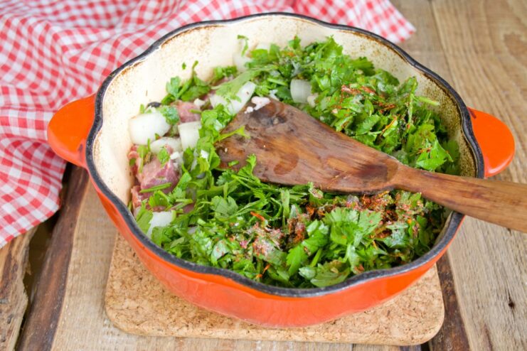 Building Layers of Flavor with Herbs, Onions, and Pork Layering fresh herbs and onions over pork in a pot before seasoning.