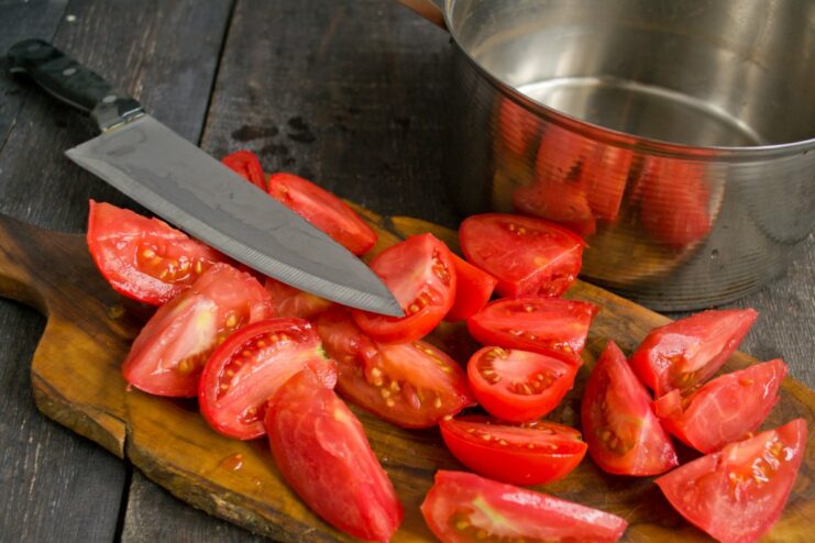 Preparing the Tomatoes: Slicing and Coring for the Stew Fresh tomatoes being cut into large chunks on a cutting board.
