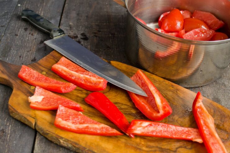 Slicing Bell Peppers for a Colorful and Flavorful Stew A red bell pepper being sliced into strips on a cutting board.