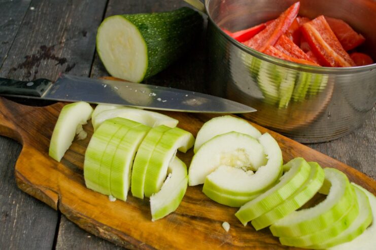 How to Cut Zucchini for the Perfect Vegetable Stew A zucchini being sliced into thick rounds on a cutting board.