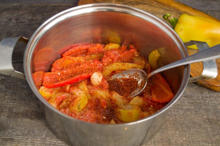 Spice It Up: Adding a Pinch of Red Pepper for Extra Heat A hand sprinkling ground red pepper into a pot of stewed vegetables.