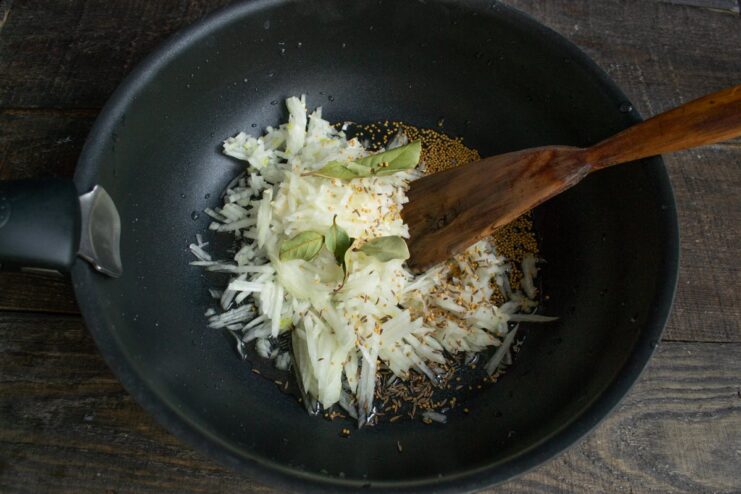 Sautéing onions with mustard and caraway seeds for a flavorful base Chopped onions, mustard seeds, and caraway seeds being sautéed in a skillet.