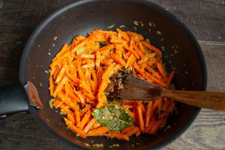 Adding carrots to the skillet to soften them with the onions Sliced carrots being added to the skillet with sautéed onions.