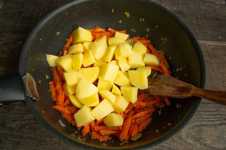 Combining potatoes with the sautéed onions and carrots Chopped potatoes being added to the skillet with carrots and onions.