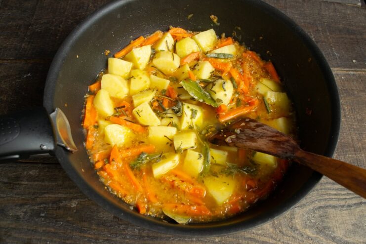 Adding liquid to the vegetables before stewing them to tenderness Pouring water into a skillet with potatoes, carrots, and onions before covering to stew.