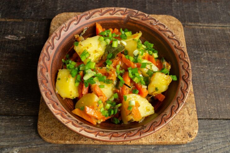 Garnishing the finished stewed potatoes with fresh green onions before serving A skillet of finished stewed potatoes with carrots and onions, garnished with chopped green onions.