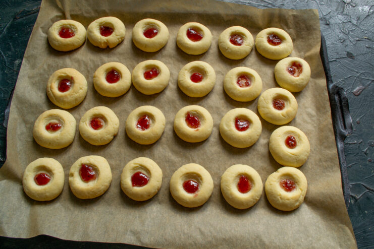 Filling the cookies with sweet cherry jam Adding a small dollop of red cherry jam into the indentation of each baked cookie.