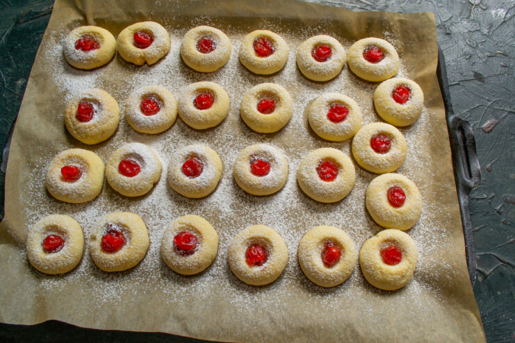 The finishing touch: adding a dried cherry Placing a single dried cherry into the jam-filled center of a vanilla cookie.