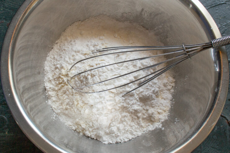 Combining flour, starch, and sugar for the cookies A whisk mixing dry ingredients like flour and sugar in a glass bowl.