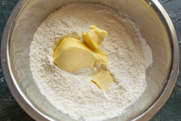 Adding softened butter to the dry ingredients Cubes of softened butter being added to the flour mixture in a bowl.