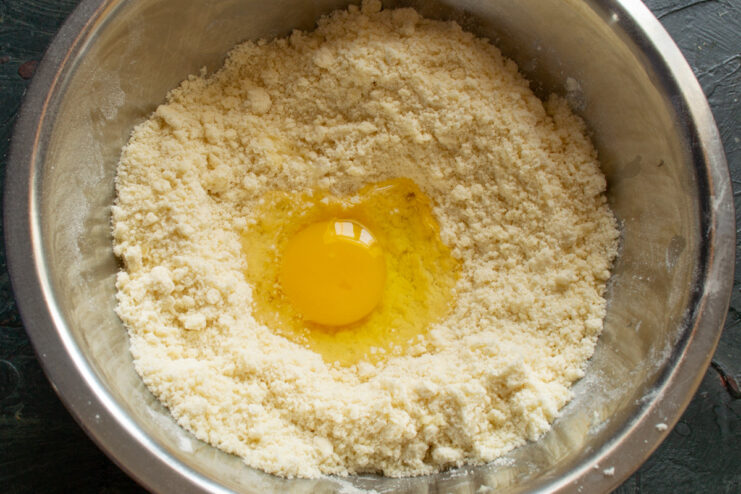 Adding an egg to bind the cookie dough A whole egg cracked into the center of the crumbly butter and flour mixture.