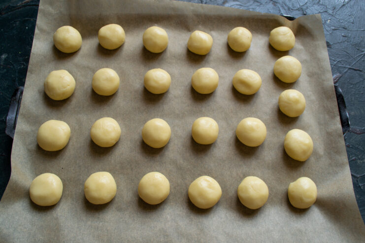 Shaping the vanilla cookies before baking Small balls of cookie dough arranged on a parchment-lined baking sheet.